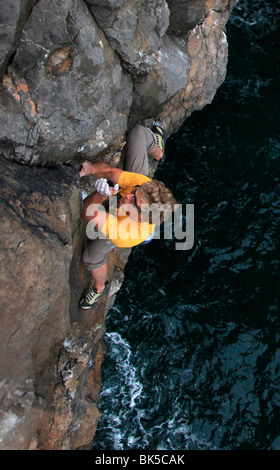 A climber deep water soloing above the sea near St. Govan's Head, South Pembrokeshire, Pembrokeshire Coast National Park, Wales Stock Photo