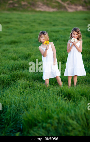 Young girls in white dresses playing in grass field Stock Photo