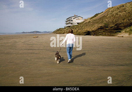 A woman walks her cocker spaniel along an eroded beach in Yachats, Oregon Stock Photo