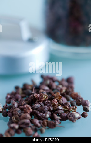 Szechuan Pepper corns in a small pile on a glass table with the jar out of focus in the background, food, spice Stock Photo