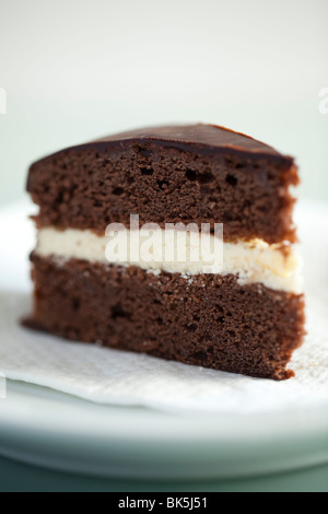 A slice of chocolate sponge cake with a fresh cream centre and chocolate ganache topping on a napkin Stock Photo