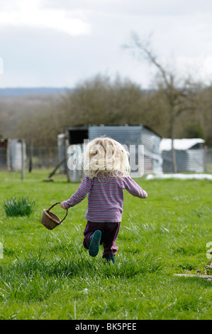 Stock photo of a 4 year old child running in the garden whilst carrying a basket. Stock Photo