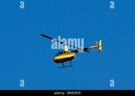 Black and yellow helicopter, Air Lloyd Robinson R44 Raven II, flying against a blue sky Stock Photo