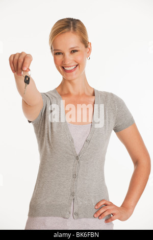 young woman holding out keys towards camera on white seamless background Stock Photo