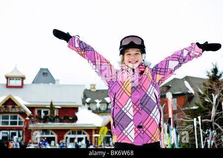 Happy teenage girl with arms raised in ski helmet at winter resort Stock Photo