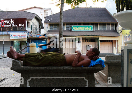 A beggar napping on a bench in Georgetown, Penang Stock Photo