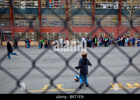 Boy kicking ball, holding book on a school playground, Manhattan, New York City Stock Photo
