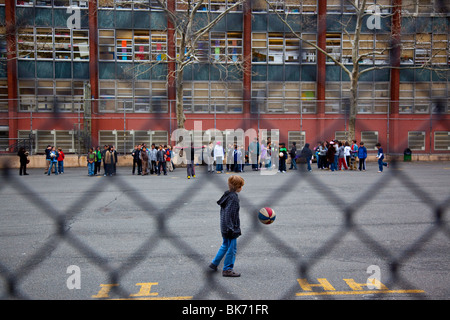 Boy kicking ball, holding book on a school playground, Manhattan, New York City Stock Photo
