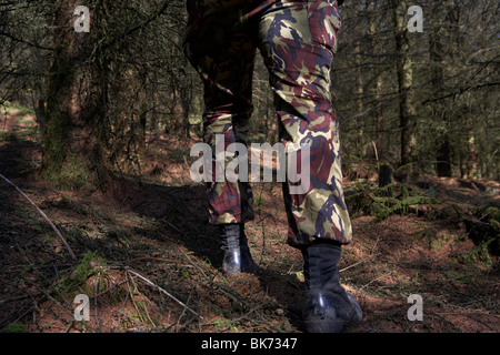 man wearing camouflage combat trousers and boots walking forward slowly in a forest in the uk Stock Photo