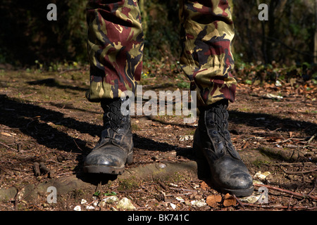 man wearing camouflage combat trousers and boots standing at ease in a forest in the uk Stock Photo