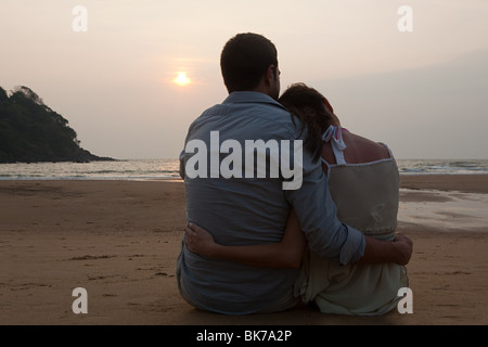 Couple sitting on beach at sunset Stock Photo