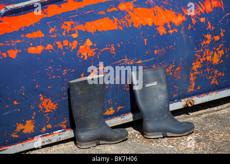 Pair of Dunlop wellington boots in front of an upturned boat with blue and orange flaking paint Stock Photo