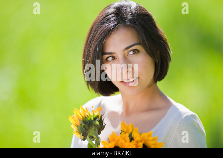 beautiful, young Hispanic woman in a grassy meadow holding flowers Stock Photo