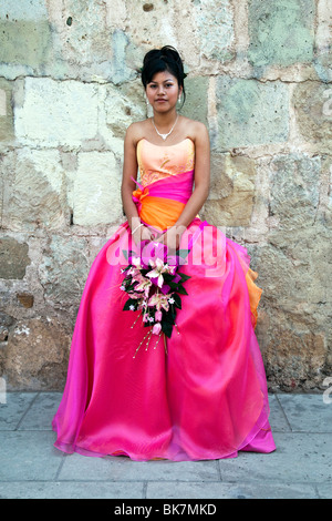 pretty dark eyed Mexican teen with upswept hair dressed in pink organza gown & carrying  pink orchids for her Quinceanera Stock Photo