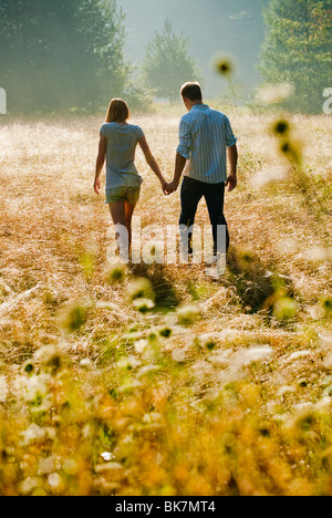 Young couple walking through field holding hands Stock Photo