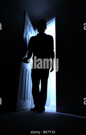 Silhouette of a male entering a dark room with a shaft of light behind Stock Photo