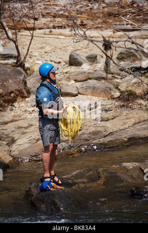 A rafting guide holding safety rope beside rushing river rapid, with ...