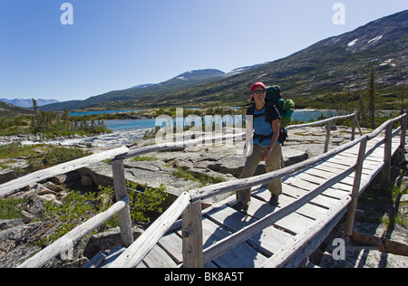 Young woman hiking, backpacking, crossing a wooden bridge, hiker with backpack, historic Chilkoot Pass, Chilkoot Trail, Deep La Stock Photo