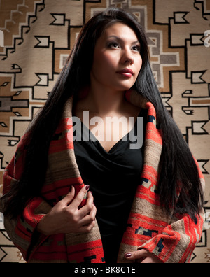 Native American woman wearing Late Classic Navajo Serape with Toadlena Two Grey Hills Textile in background. Stock Photo