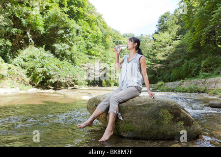 Young Woman Drinking Water at River Stock Photo