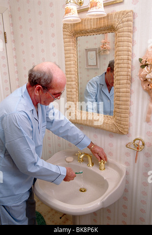 Elderly man in his pyjamas brushing his teeth in his bathroom. Stock Photo