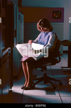 Female programmer reviews reports in the computer main frame room of a medium size company. Stock Photo