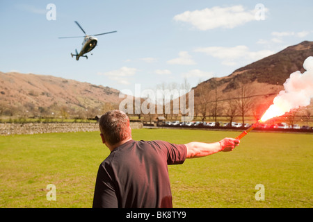 A member of Langdale/Ambleside Mountain Rescue Team uses a flare to alert an approaching air ambulance to the landing site Stock Photo