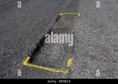 pothole in the middle of a tarmac road in the uk caused by frost damage in cold weather marked for repair with yellow paint Stock Photo