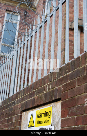 Razor wire security fence on top of brick wall surrounding an urban building. Stock Photo