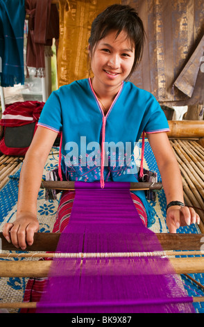 Young woman weaving cloth on loom; Patara Elephant Farm, Chiang Mai Province, Thailand. Stock Photo