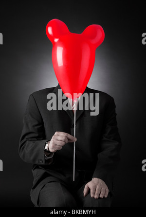 businessman in gray suit holding red mouse head shaped balloon in front of his face Stock Photo