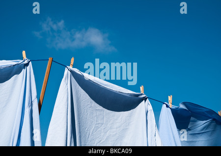 Shirts hanging out to dry with blue sky and one small cloud. Stock Photo