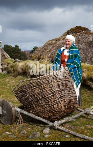 Woman (MR in Traditional dress, woven basket & thatched Scottish croft at Highland Folk Museum, Visitor Attraction, Newtonmore, Speyside, Scotland, UK Stock Photo