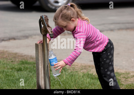 Young caucasian girl fills water bottle from pump Stock Photo