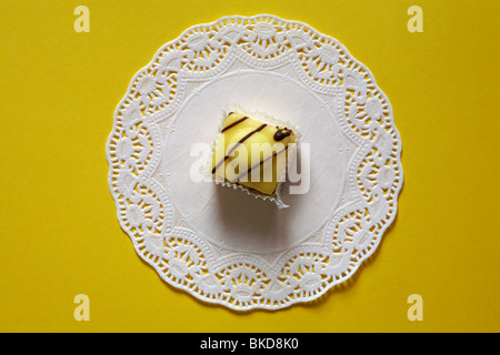 Special Edition Lemon French Fancies by Mr Kipling on white doily set on yellow background Stock Photo