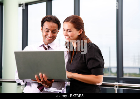 Asian male and white female office workers in contemporary office environment using laptop. Stock Photo