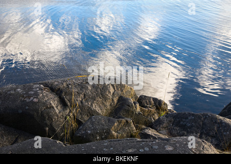 Black rock over white clouds reflected in water. Stock Photo