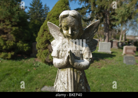 A statue of an angelic child is frozen in time with  its' hands clasped in silent prayer. Stock Photo