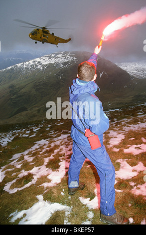 A mountain rescue member uses a flare to attract an approaching sea king helicopter to the casualty site, Lake District Stock Photo
