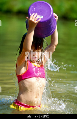 Young girl pours a bucket of cool water over her head on hot summer day in lake, Midwest USA Stock Photo