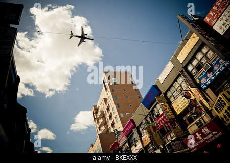 An airliner flies low over 40th Avenue, Flushing, New York USA on route to land at La Guardia Airport New York Stock Photo