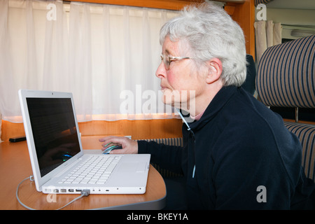 Senior woman pensioner using wifi on a MacBook laptop computer inside a motorhome. England UK Britain Stock Photo