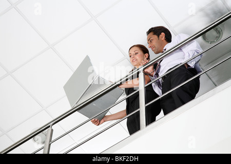 Asian male and white female office workers in contemporary office environment using laptop. Stock Photo