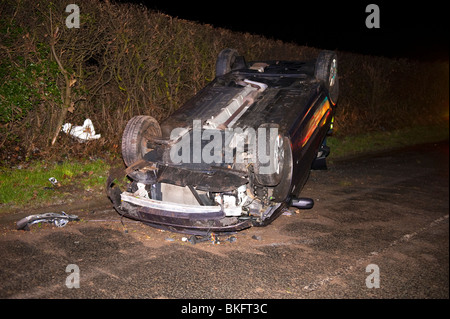 Car crashed on roof on icy winter country lane Stock Photo