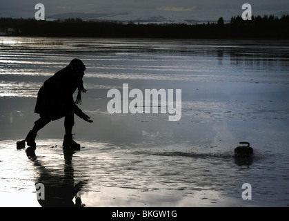 A curler casts his stone on the frozen lake Menteith in Stirlingshire Scotland during a prolonged spell of freezing weather Stock Photo