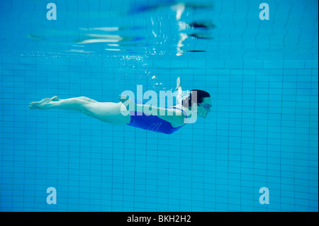Woman in blue swimming costume swimming under water in pool Stock Photo