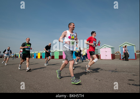 Runners pass brightly painted beach huts at Hove during the last few miles of the Brighton Marathon Stock Photo