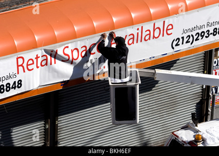 Worker attaching sign, advertising space for rent on Nostrand Avenue, Flatbush, Brooklyn, NYC Stock Photo
