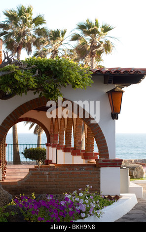 Flowers and palm trees surround a walkway covered by Spanish arches. Stock Photo