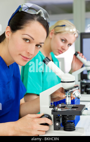 A female medical or scientific researcher or doctor using her microscope in a laboratory with her colleague. Stock Photo